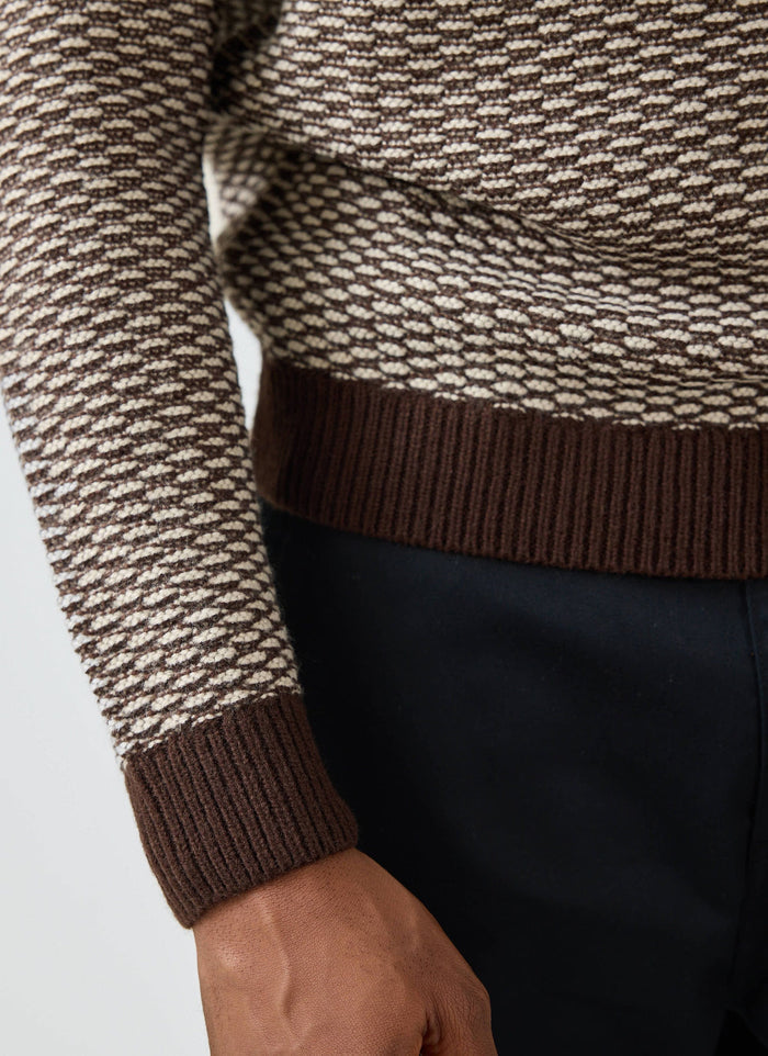 A close-up of a model wearing the Percival Charlestown Knitted Jumper in chocolate and beige, with his hands in his pockets.