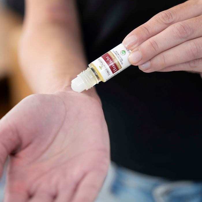 Close-up of person applying Headache roll-on oil to inner wrist against a dark blurred background