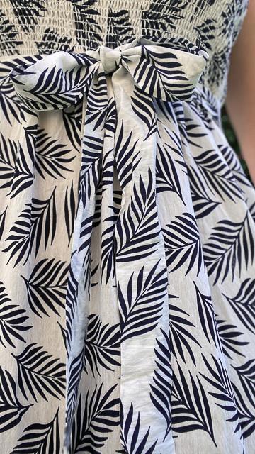 Close-up of white maxi dress with black tropical leaf print and smocked waist bow detail