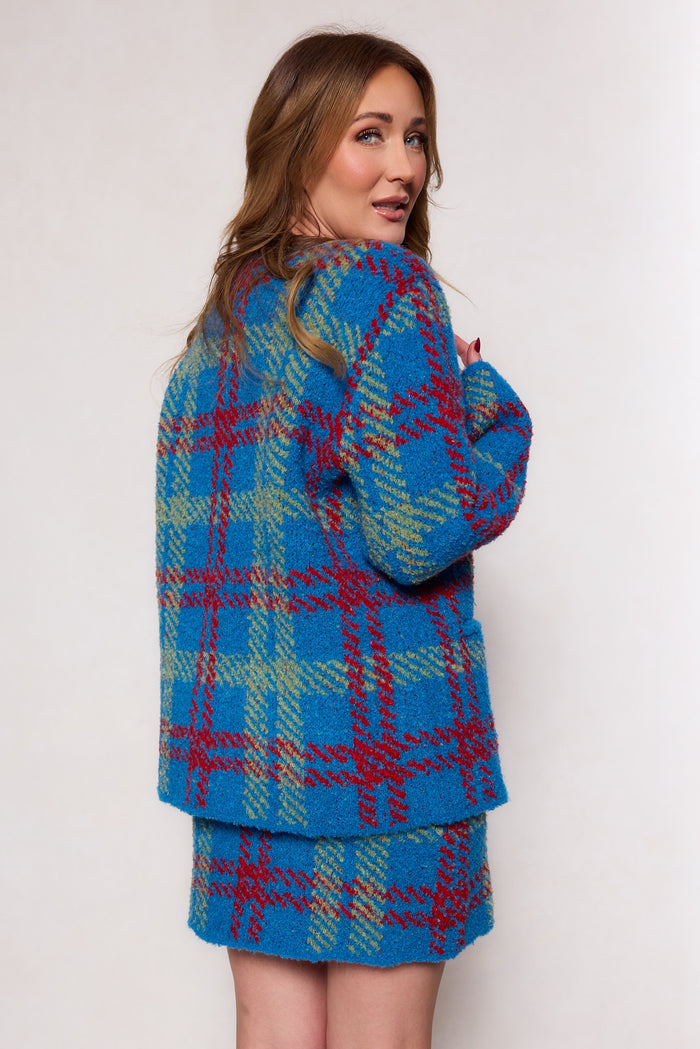 A woman with wavy, light brown hair poses sideways wearing the Ivy City Co Solomon Set in Blue Plaid, featuring red and green patterns in a structured fit, styled against a plain light background.
