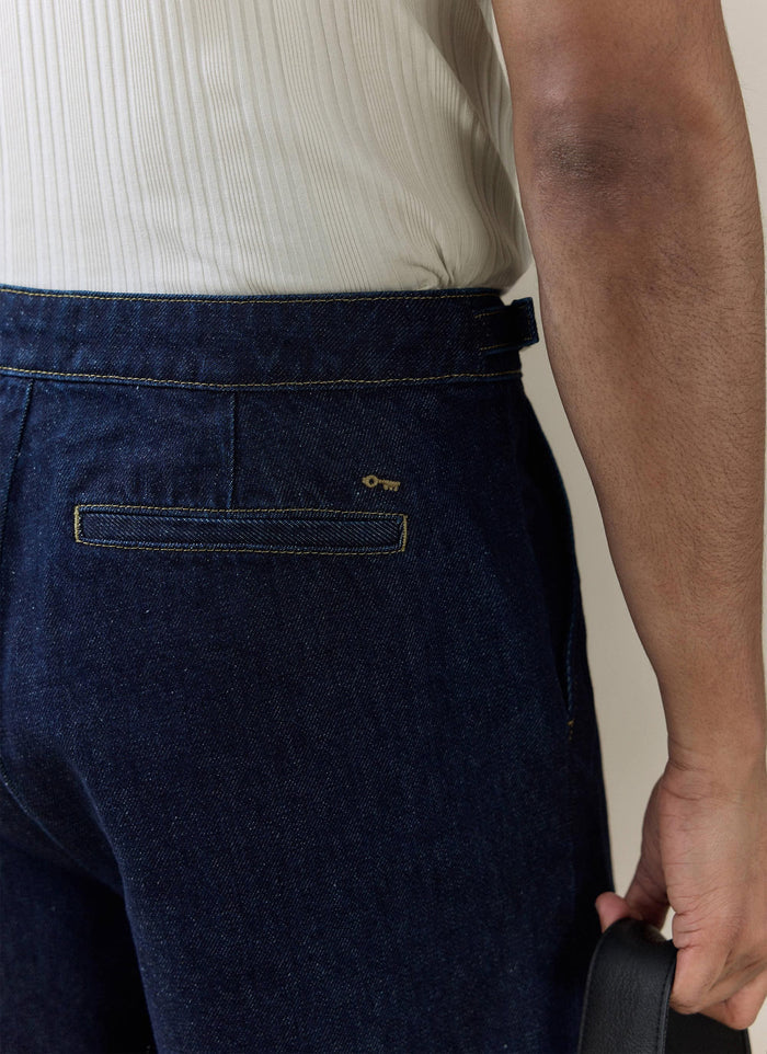 Percival Blake Double Pleated Denim Shorts in dark indigo, featuring an embroidered key logo and contrast-stitched pocket.