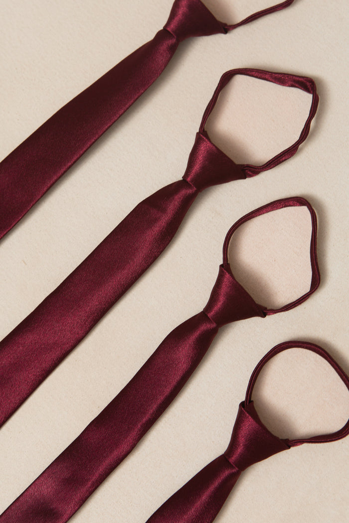 Four Ivy City Co Boys Max Ties in Wine Satin are arranged side by side on a light beige surface, each tied simply with loops at the top—an ideal accessory for fall weddings.