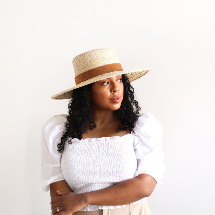 Woman wearing a straw hat and white top against a plain background