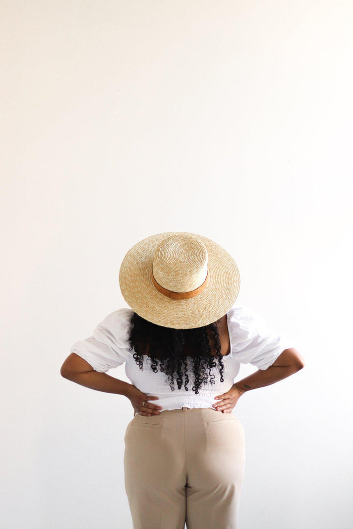Person wearing a straw hat and white shirt with beige pants on a light background