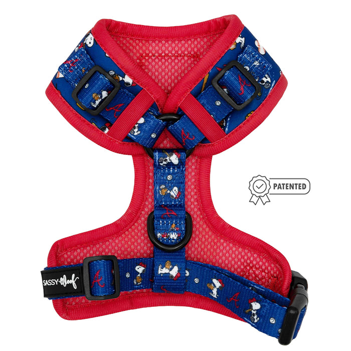 The Sassy Woof Dog Adjustable Harness - MLB™ x Peanuts™ Atlanta Braves™ features blue and red design, Peanuts characters, Atlanta Braves logos, black adjustable straps, secure buckles, and a “PATENTED” badge icon.