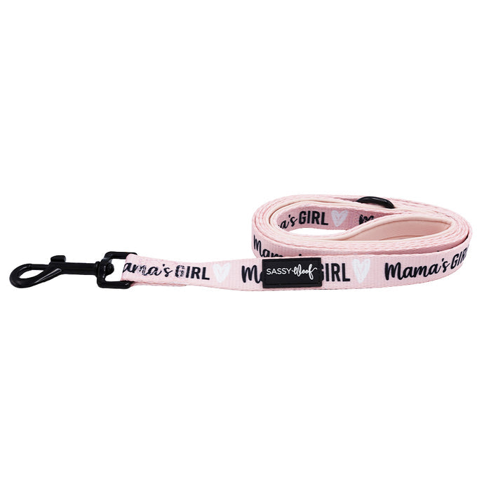 The Sassy Woof Dog Leash - Mama's Girl features pink neoprene, black hardware, “Mamas GIRL” text with white hearts, and a label near the clip. Pair it with the matching harness or collar for a coordinated look.