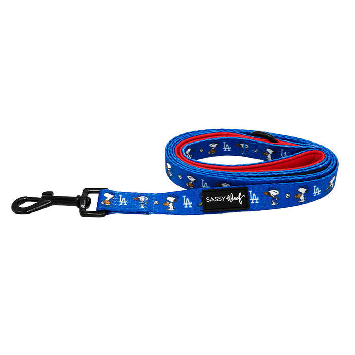 The Sassy Woof Dog Leash - MLB™ x Peanuts™ Los Angeles Dodgers™ is blue with a red underside, features cartoon dog characters, white LA logos, a black metal clasp, and a Sassy Woof label.