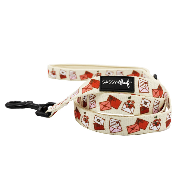 The Sassy Woof Dog Leash - P.S. I Woof You is cream-colored with red and pink love letters, a black metal clip, and a Sassy Woof label. Pair it with our matching dog harness for an adorable accessory set!.