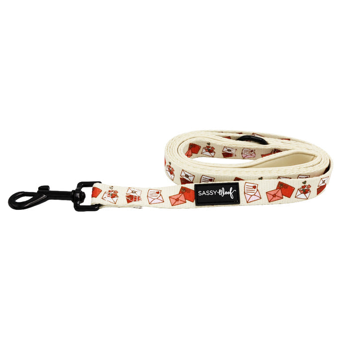 The Sassy Woof "P.S. I Woof You" dog leash features a cream base with red and pink envelope prints, a black metal clasp, and the signature Sassy Woof label—perfect to pair with matching harnesses or accessories.