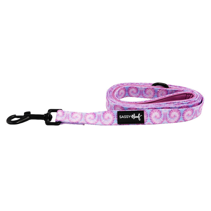 The Sassy Woof Dog Leash - Purple Haze features a pink and purple tie-dye pattern, black metal clasp, comfy neoprene handle, and brand label. Pair it with the matching harness for a stylish walk.