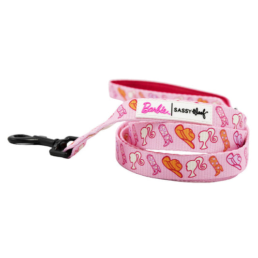 The Sassy Woof Dog Leash - Western Barbie™ is pink with yellow, orange, and pink Barbie silhouettes and accessories, inspired by Western Barbie. It features a black metal clasp and stylish branding throughout.