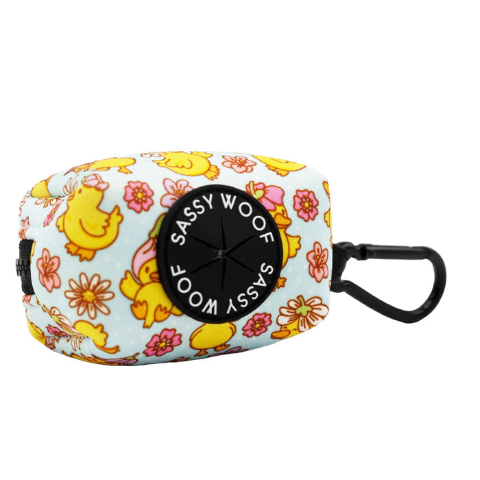 The Sassy Woof Dog Waste Bag Holder - Good Duck, Babe! features a cute duck and pink flower design, a black circular dispenser, and clip—perfect for pairing with a matching harness or other duck-themed accessories.