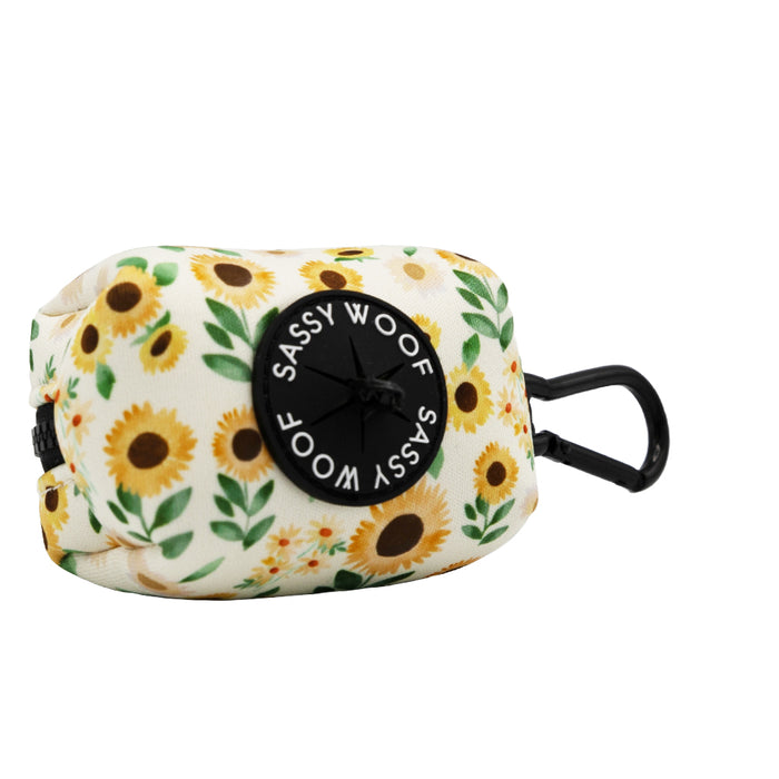 The Sassy Woof Dog Waste Bag Holder - Sunflower Dreams is a small, rectangular bag with a black logo and clip—ideal for attaching to a leash or bag and pairing with the matching dog harness set.