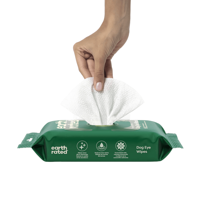 White background with a hand pulling a Earth Rated Pet Eye wipe from a green packet.