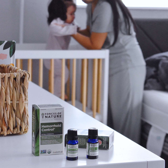 Forces of Nature Hemorrhoid Control box and two blue bottles on a white dresser with parent holding baby blurred behind