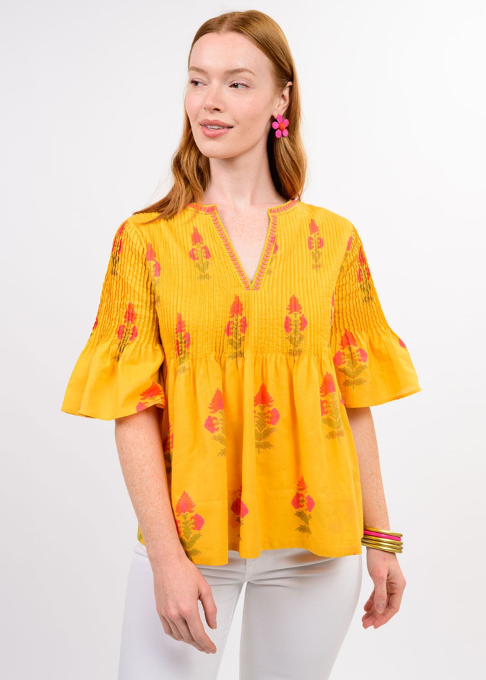Woman wearing a yellow v-neck top with a floral print and white jeans