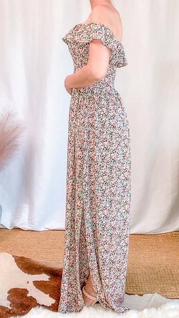 Woman wearing a floral off-shoulder maxi dress with side slit, standing in a minimalist indoor setting