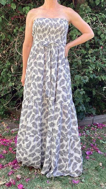 Woman wearing a strapless white maxi dress with black tropical leaf print, standing in garden with greenery and flower petals