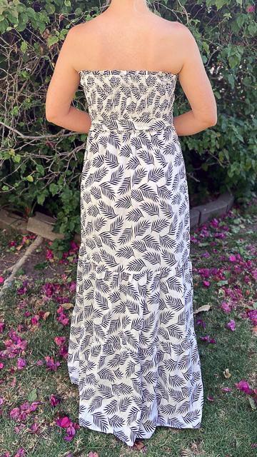 Back view of woman wearing white tropical print strapless maxi dress with black leaf patterns in garden setting