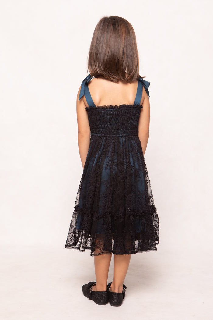 Young girl wearing a black lace dress with blue straps on a white background
