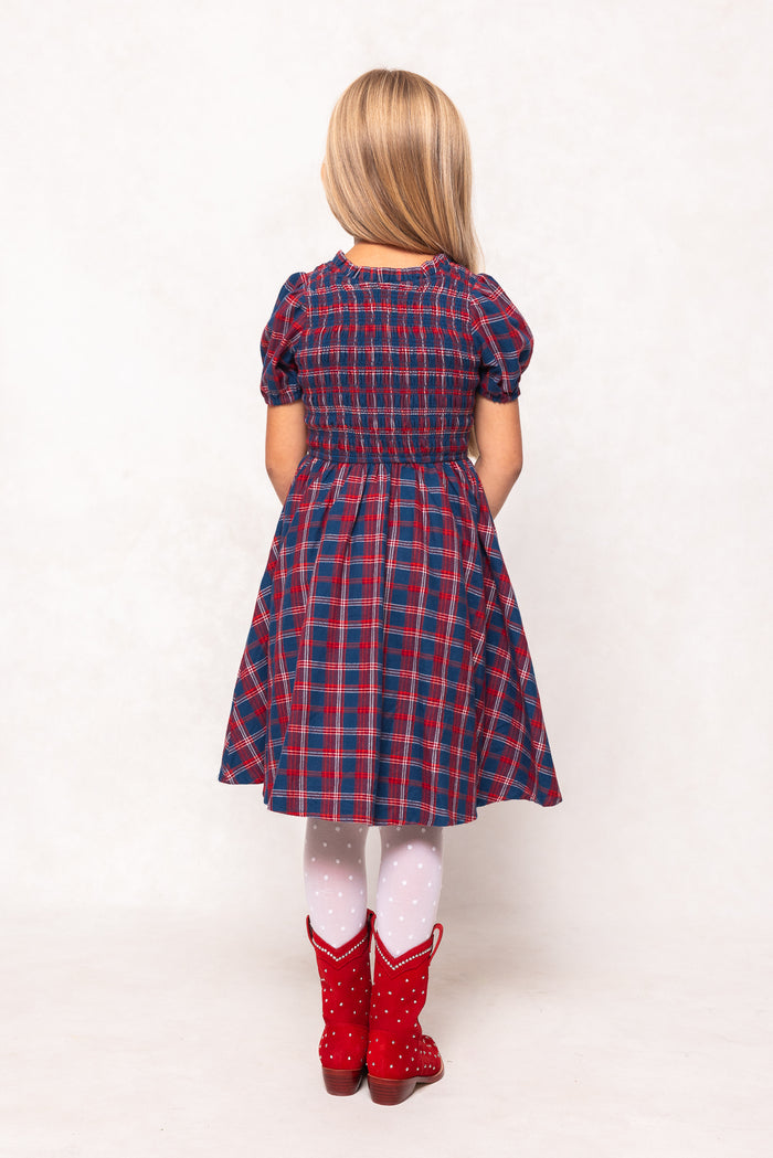 Person wearing a red and blue plaid dress with white tights and red boots on a white background