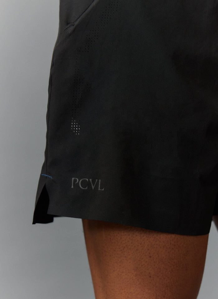 A close-up of the Percival PCVL Performance Shorts in black, showing the tonal PCVL logo, side split hem, and perforations.