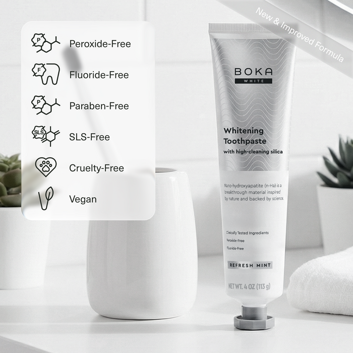 Boka White Whitening Toothpaste tube standing upright on a white surface next to a white cup, with a feature callout panel listing Peroxide-Free, Fluoride-Free, Paraben-Free, SLS-Free, Cruelty-Free, and Vegan.