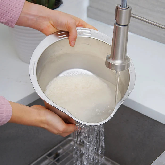 Person washing rice in a metal bowl under running water from a faucet.
