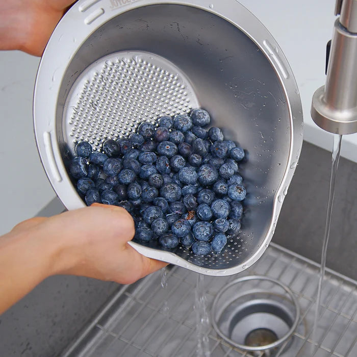 Person washing blueberries in a colander under running water in a kitchen sink.