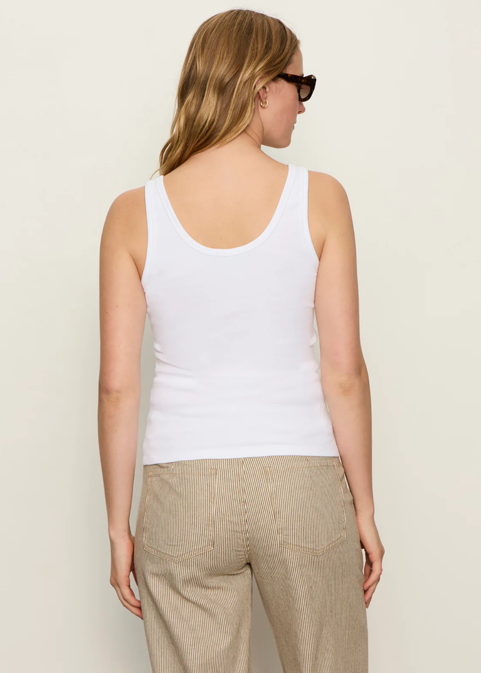 Woman turned aorund wearing a white lace up tank with striped pants
