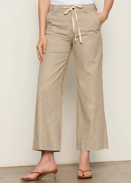 Woman wearing brown and white striped wide leg pants with sandals and a white tank top
