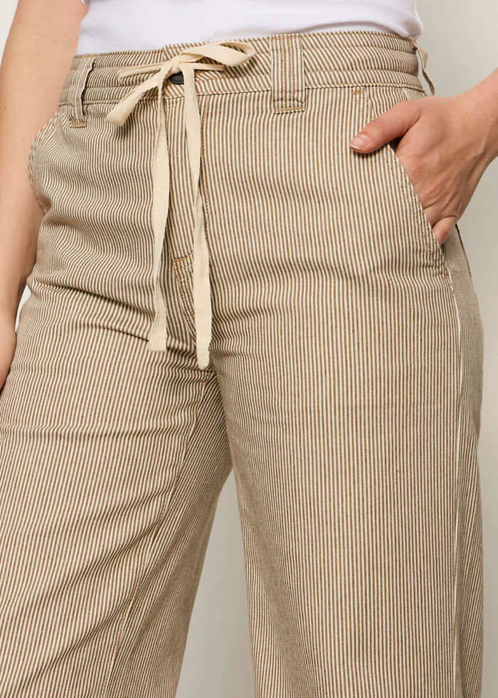 Woman wearing brown and white striped wide leg pants with sandals and a white tank top