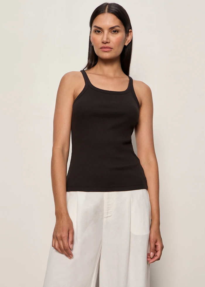 Woman wearing a black tank top with white bottoms and a brown belt