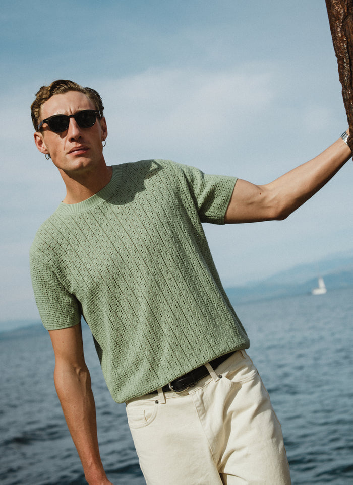Percival Siena knitted T-shirt in pistachio green pointelle cotton, worn by a model outdoors by the sea.