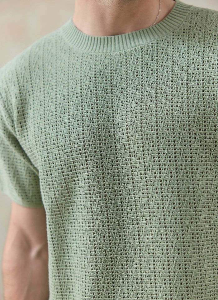 Close-up of the pistachio Percival Siena Knitted T Shirt on a model, highlighting the detailed cotton pointelle stitch.
