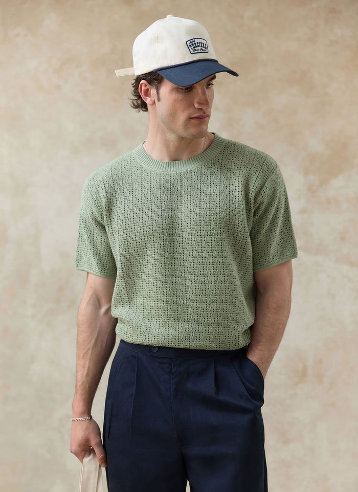 The Percival Siena Knitted T Shirt in pistachio green, a pointelle cotton knit styled on a model with navy trousers.