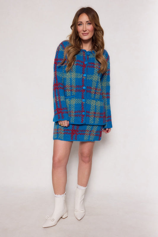 A woman with long wavy hair models the Ivy City Co Solomon Set in Blue Plaid—a structured jacket and matching skirt—paired with white ankle boots and frilly socks, against a plain white background.