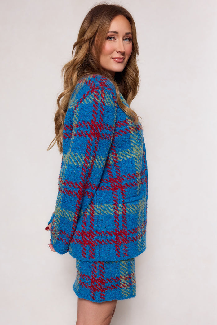 A woman with long wavy hair wears the Ivy City Co Solomon Set in Blue Plaid, featuring a structured fit, as she stands sideways and smiles at the camera against a plain light background.