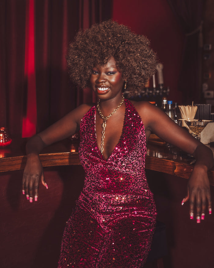 Woman in a red sequin 70s  disco jumpsuit posing in a bar setting