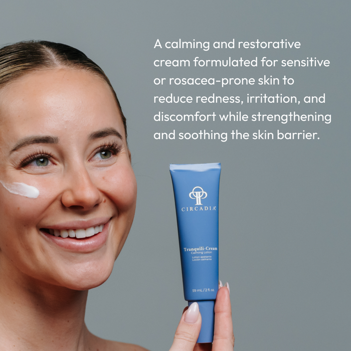 Smiling woman with smooth skin applying a white cream to her cheek, holding a blue tube of Tranquili-Cream | Circadia, skincare lotion for sensitive or rosacea-prone skin.