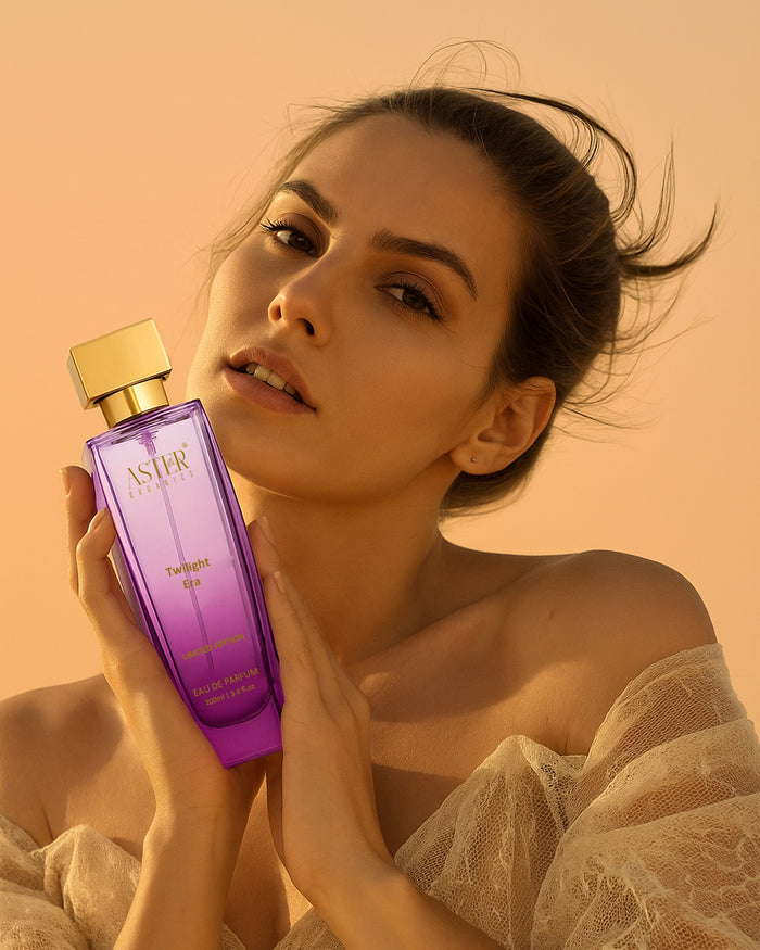 Woman holding a purple ASTER perfume bottle against a warm beige background