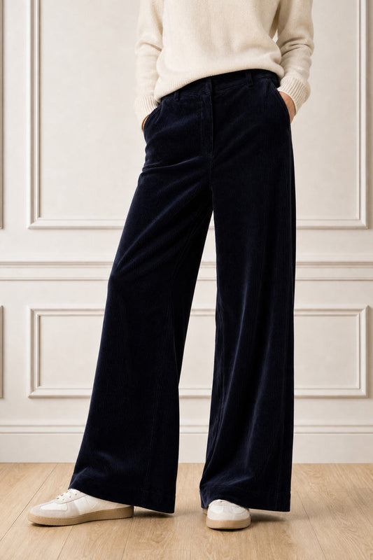 Model wearing the Aspiga Wide Leg Chunky Corduroy Trouser in Deep Navy with a cream jumper and white trainers, cropped front view